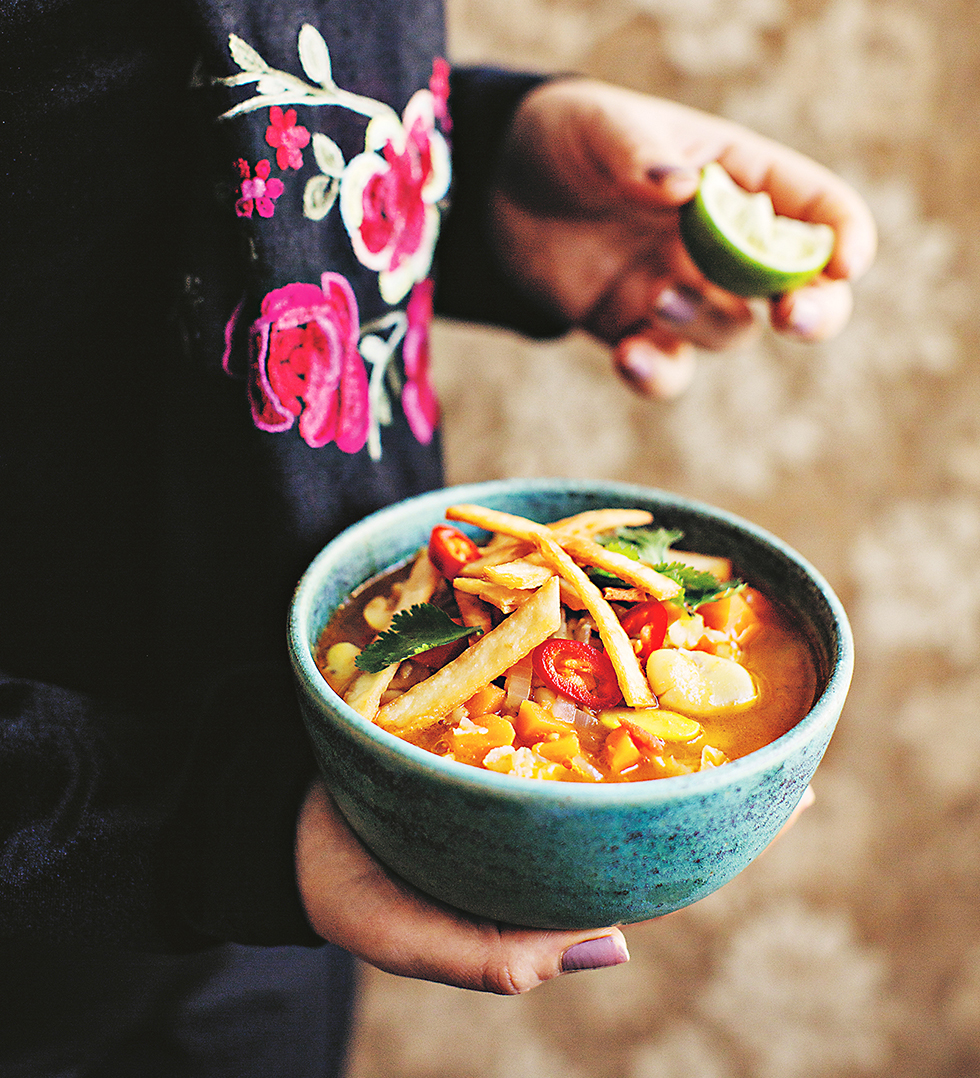 En hand håller en skål med mexikansk soppa.